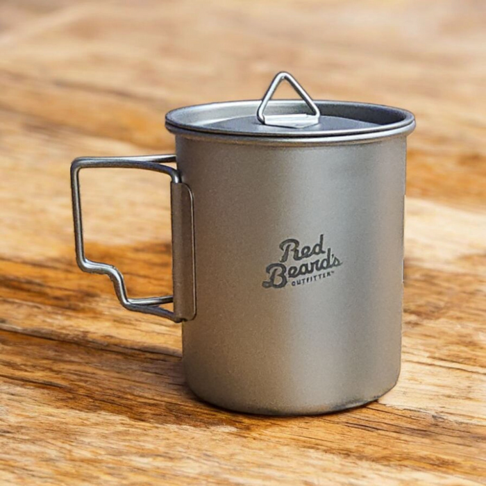 Red Beard’s Outfitter 450 mL titanium camping mug with fitted lid on a wooden surface