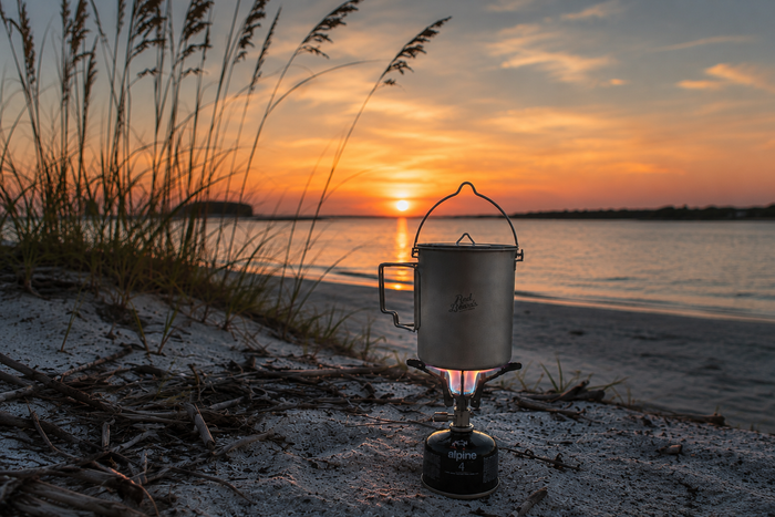 Red Beard’s Outfitter 750 mL titanium backpacking pot heating on a camp stove at sunset